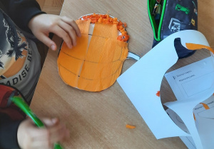 Dzieci wykonują prace plastyczne przy użyciu czarnego kartonu - kot, pomarańczowej bibuły - dynia, białej bibuły – duszek, czarnej bibuły – nietoperz, czarnego kartonu – pająki, zielonej kartki - listki.