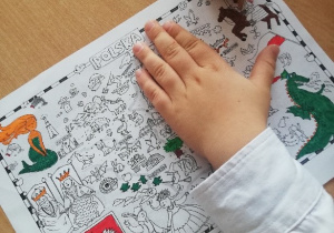 Dzieci malują kolorowankę przedstawiającą mapę Polski z zaznaczonymi na niej ważnymi miejscami dla naszego kraju.