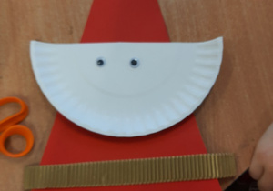 Dzieci wykonują postać Mikołaja z czerwonego kartonu, papierowego białego talerzyka i innych drobnych dodatków.
