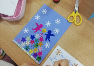 Dzieci wykonują świąteczne kartki z kartonów i kolorowych kartek, ozdabiają je świecącymi gwiazdkami i śnieżynkami. Powstają wesołe renifery, bałwanki, mikołaje, aniołki, bombki. Dzieci piszą własnoręcznie świąteczne życzenia.