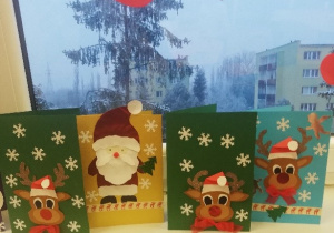 Prezentacja prac dzieci. Na kartkach są świąteczne motywy: aniołki, renifery, mikołaje, bombki, gwiazdki i śnieżynki. Każda kartka ma własnoręcznie napisane przez dzieci życzenia.