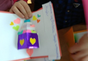 Dzieci prezentują laurki wykonane z kartonu, kwiaty wykonane z kolorowych kartek ksero. Pojedyncze kwiaty sklejone w bukiet. Druga laurka wykonana jest z kartonu z ponaklejanymi kolorowymi serduszkami.