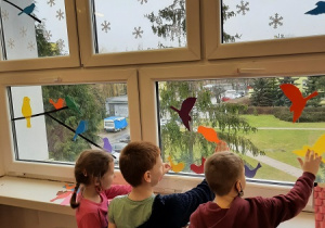 Dzieci pomagają w dekorowaniu świetlicy. Na oknach naklejają kolorowe ptaki wycięte z kartonów.