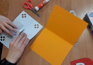 Dzieci wykonują kartki walentynkowe przy użyciu różnych materiałów: kolorowych serduszek, kartonów, taśmy ozdobnej.