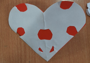 Dzieci prezentują wykonane przez siebie kartki walentynkowe. Zrobione są z czerwonego kartonu i białej kartki ksero wyciętych w kształcie serca.