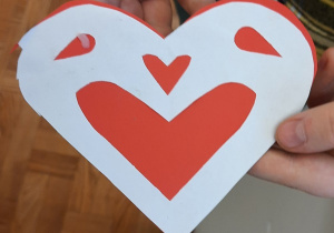 Dzieci prezentują wykonane przez siebie kartki walentynkowe. Zrobione są z czerwonego kartonu i białej kartki ksero wyciętych w kształcie serca.