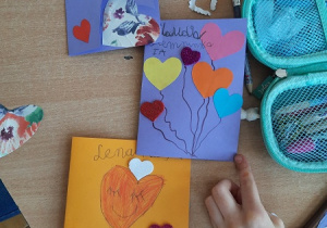 Dzieci prezentują wykonane przez siebie kartki walentynkowe. Walentynki zrobione są przy użyciu różnych materiałów: kolorowych i brokatowych serduszek, kartonów, taśmy ozdobnej.