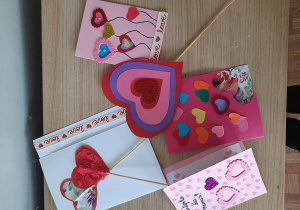 Dzieci prezentują wykonane przez siebie kartki walentynkowe. Walentynki zrobione są przy użyciu różnych materiałów: kolorowych i brokatowych serduszek, kartonów, taśmy ozdobnej.