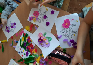 Dzieci wykonują wiosenne kwiaty. Kawałki kolorowej bibuły naklejają na wcześniej przygotowane szablony kwiatów.
