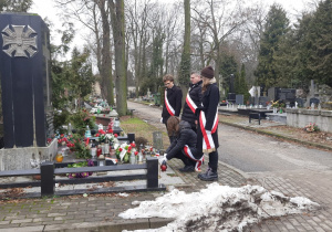 Uczniowie wraz z nauczycielem składający znicze przy symbolicznych mogiłach - pomnikach AK i Szarych Szeregów.