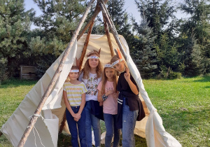 4 dziewczynki z klasy 4b schowały się w zbudowanym przez siebie tipi. Stoją, są radosne.