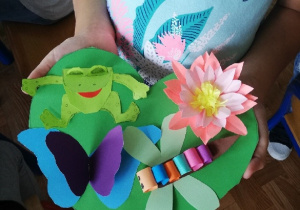 Prace plastyczne wykonane z papieru przedstawiające kolorowe kwiatki, żabki, motylki.