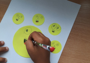 Dzieci wykonują prace plastyczne z żółtych papierowych kółek, na których rysują swoje emocje.