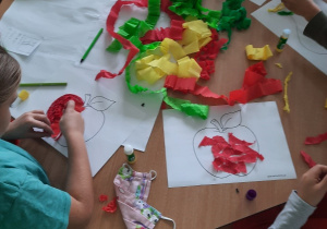 Dzieci wyklejają narysowane gruszki i jabłka kawałkami bibuły