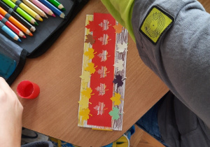 Dzieci przy użyciu kredek i kartonowych elementów wykonują zakładkę do książki o tematyce jesiennej.