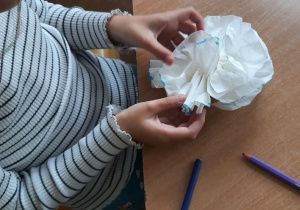 Dziewczynka wykonuje kwiatka z białej serwetki.