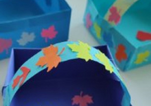 prace plastyczne - koszyczki wykonane z kolorowego kartonu, na których ponaklejane są kolorowe listki i serduszka wycięte z papieru.