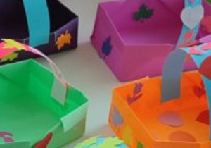 prace plastyczne - koszyczki wykonane z kolorowego kartonu, na których ponaklejane są kolorowe listki i serduszka wycięte z papieru.