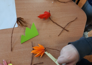 Dzieci wykonują listki z kolorowego papieru składając go w harmonijkę, doczepiają ogonek wykonany ze skręconej brązowej bibuły.
