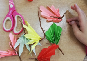 Dzieci wykonują listki z kolorowego papieru składając go w harmonijkę, doczepiają ogonek wykonany ze skręconej brązowej bibuły.