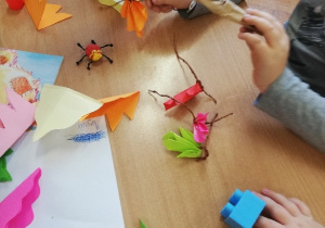 Dzieci doklejają przygotowane papierowe listki do gałązki wykonanej ze skręconego papieru pakowego.